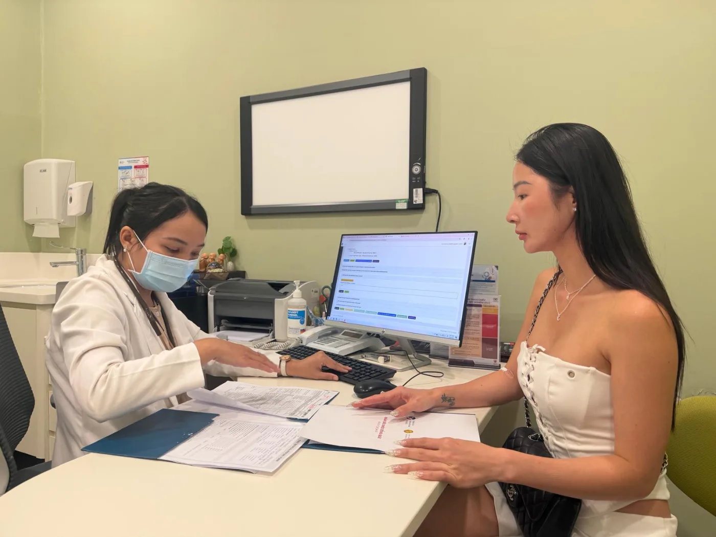 Anna seated with a doctor who is going through paperwork during a consultation
